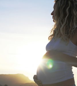Beautiful pregnant woman holds her belly at the beach during sunset.
